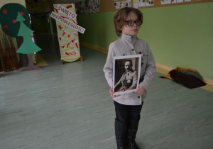 Uczeń w mundurze legionisty trzyma portret Piłsudskiego.