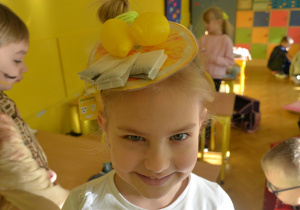 Portret dziewczynki przebranej za herbatę ekspresową. Na głowie kapelusz z herbatą ekspresową i cytrynami.